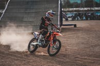 越野摩托车活动令人兴奋，骑行在泥土路上，留下灰尘痕迹，背景是坡道