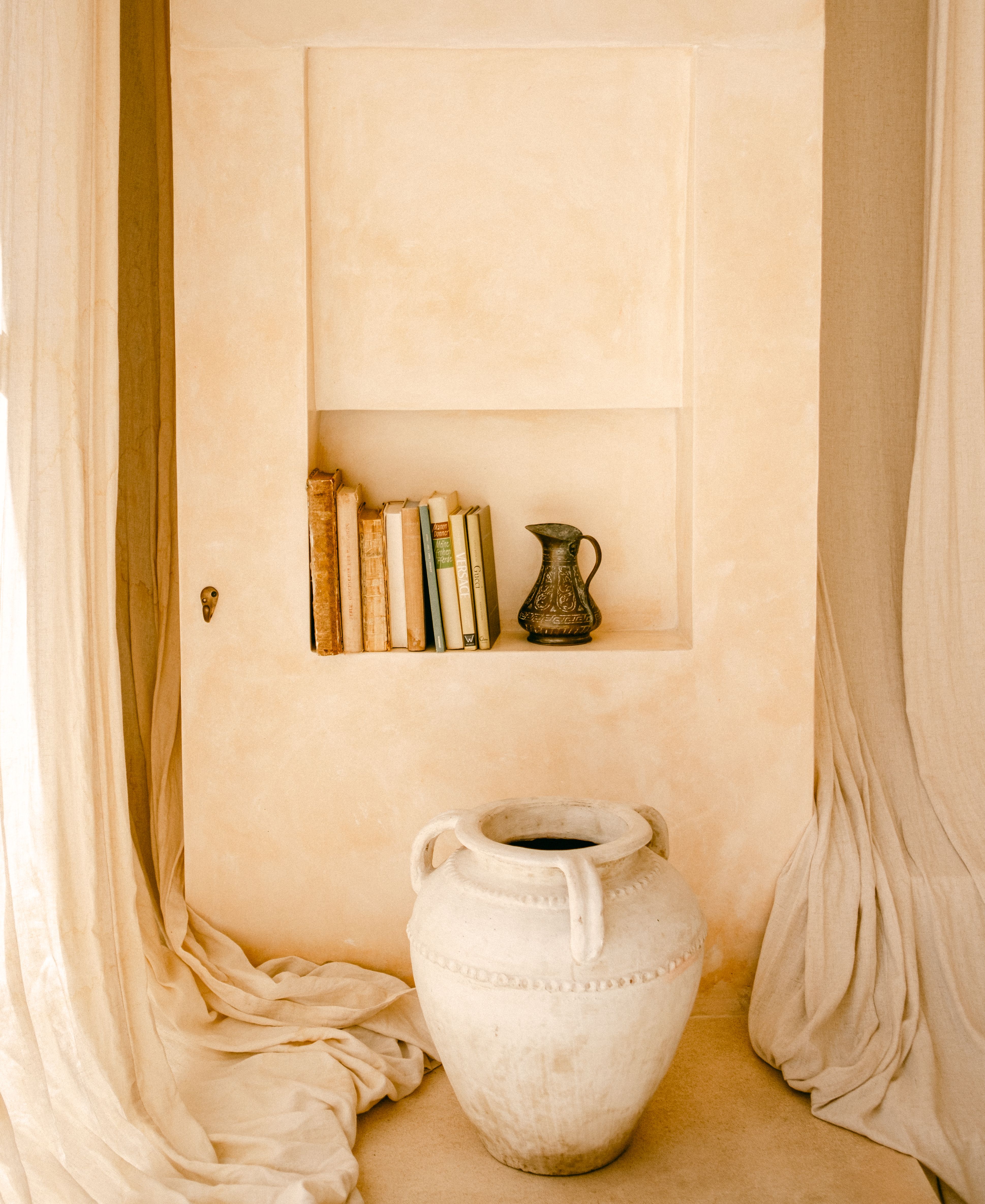 Aesthetic interior with rustic books, vase, and jug in soft warm tones.