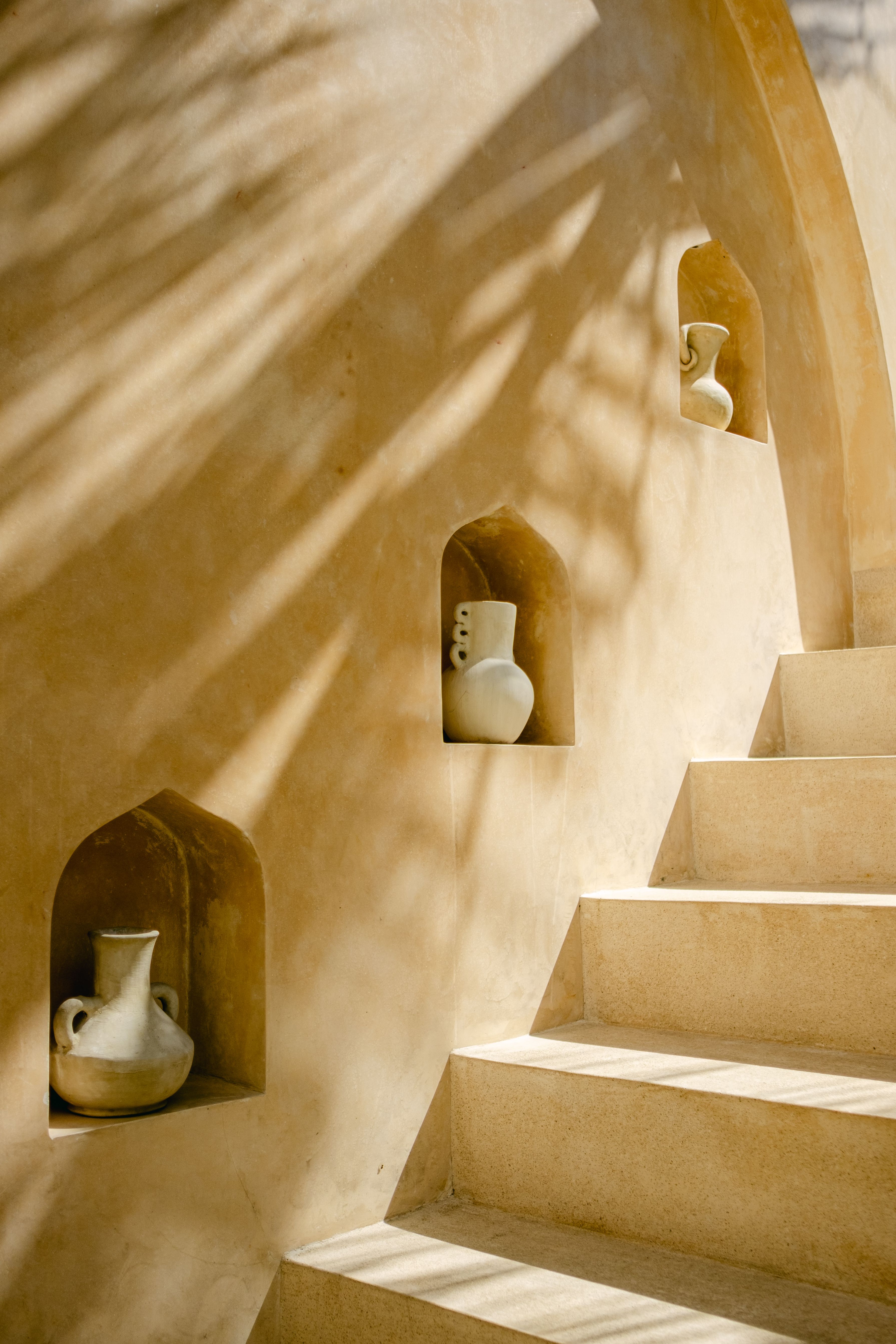 A minimalist staircase with ceramic jugs in an artistic setting, emphasizing natural sunlight and shadows.