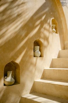 A minimalist staircase with ceramic jugs in an artistic setting, emphasizing natural sunlight and shadows.