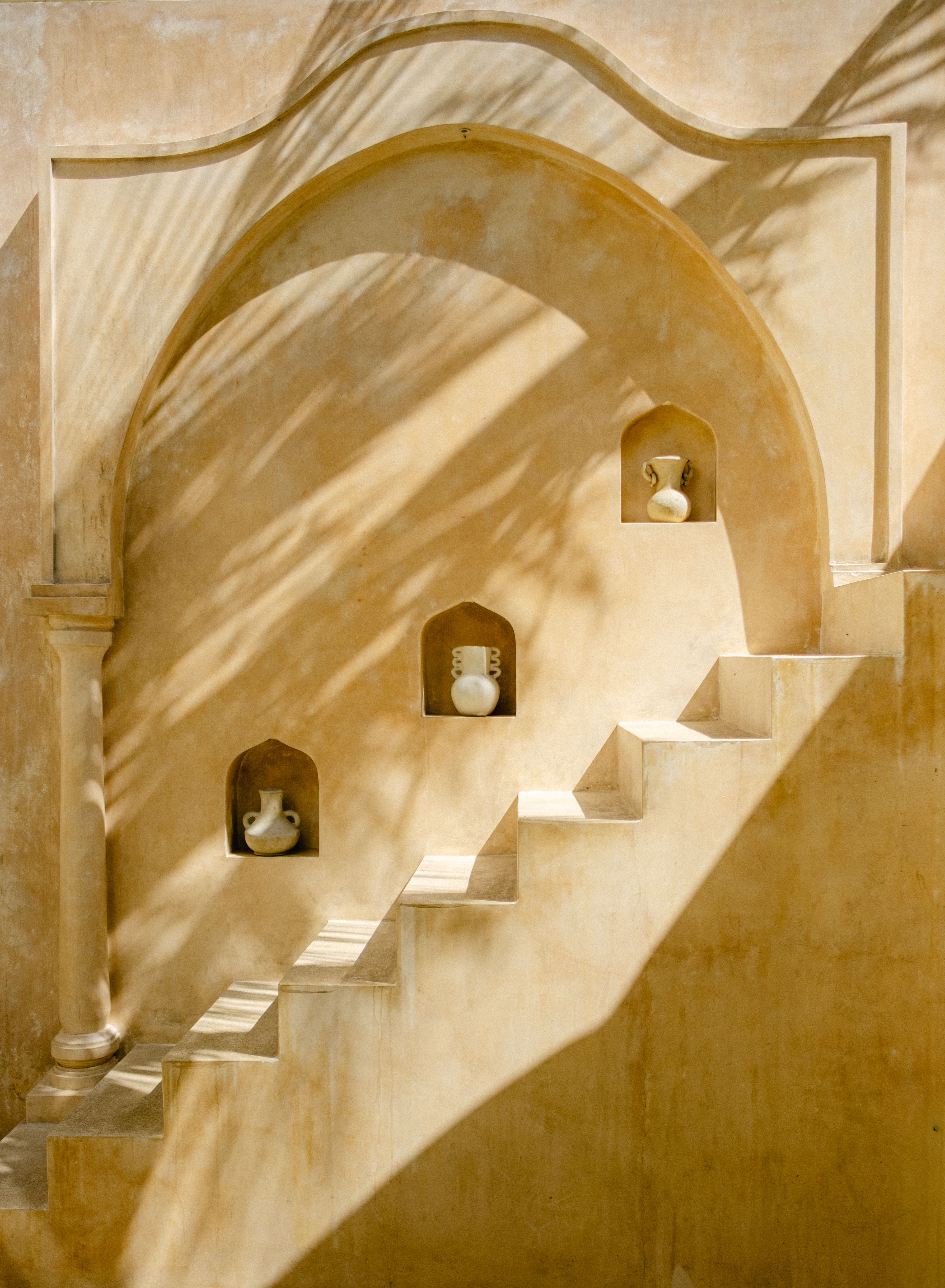 Rustic staircase with vases in wall niches, casting artistic shadows.