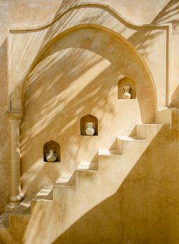 Rustic staircase with vases in wall niches, casting artistic shadows.