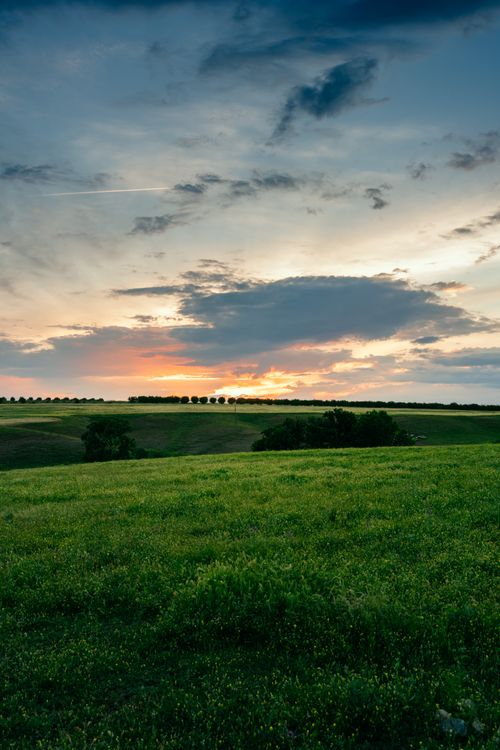 Free Serene landscape with lush green fields under a dramatic sunset sky, capturing the tranquility of nature. Stock Photo