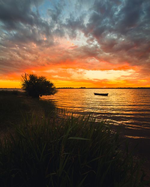 Free A tranquil sunset scene with a boat silhouetted on a river in Uruguay, vibrant orange sky. Stock Photo