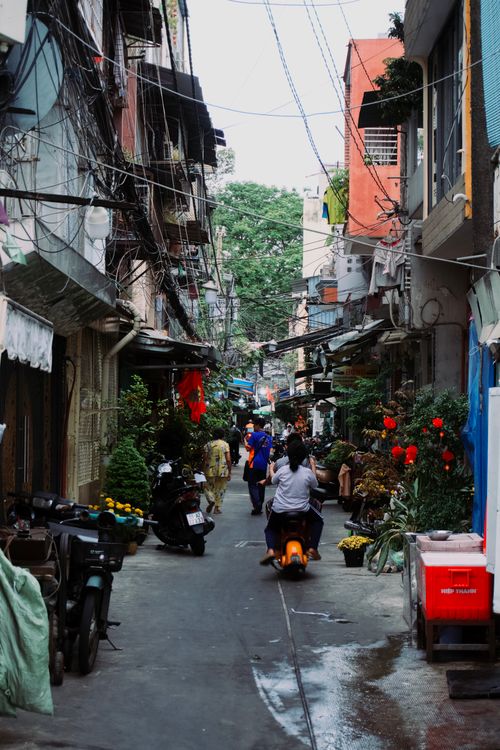 Free A lively city alley with people and scooters showcasing everyday urban life and colorful street displays. Stock Photo