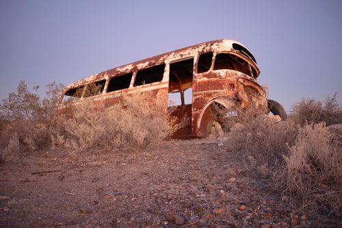 Free Weathered and rusted bus in a desert setting amidst dry bushes under a clear sky. Stock Photo