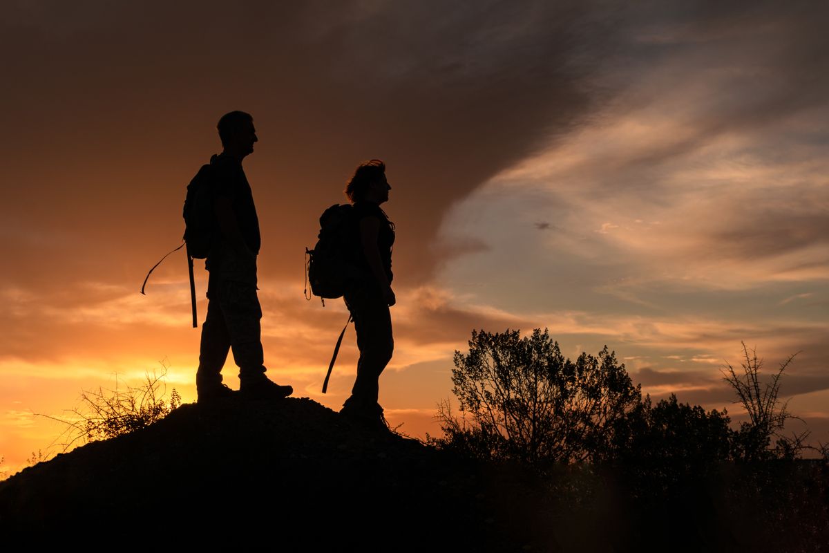 Two hikers with backpacks on a hilltop at sunset