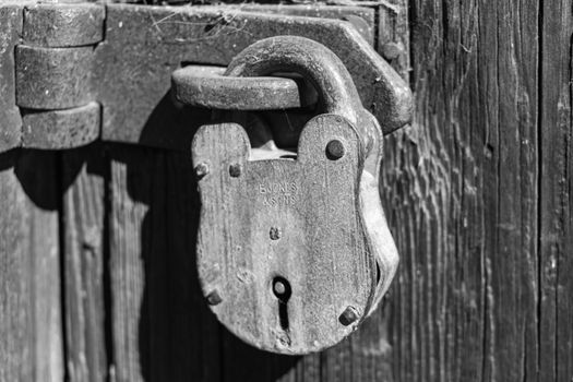 Close-up of an old rustic padlock on a weathered wooden door, capturing vintage charm and texture.
