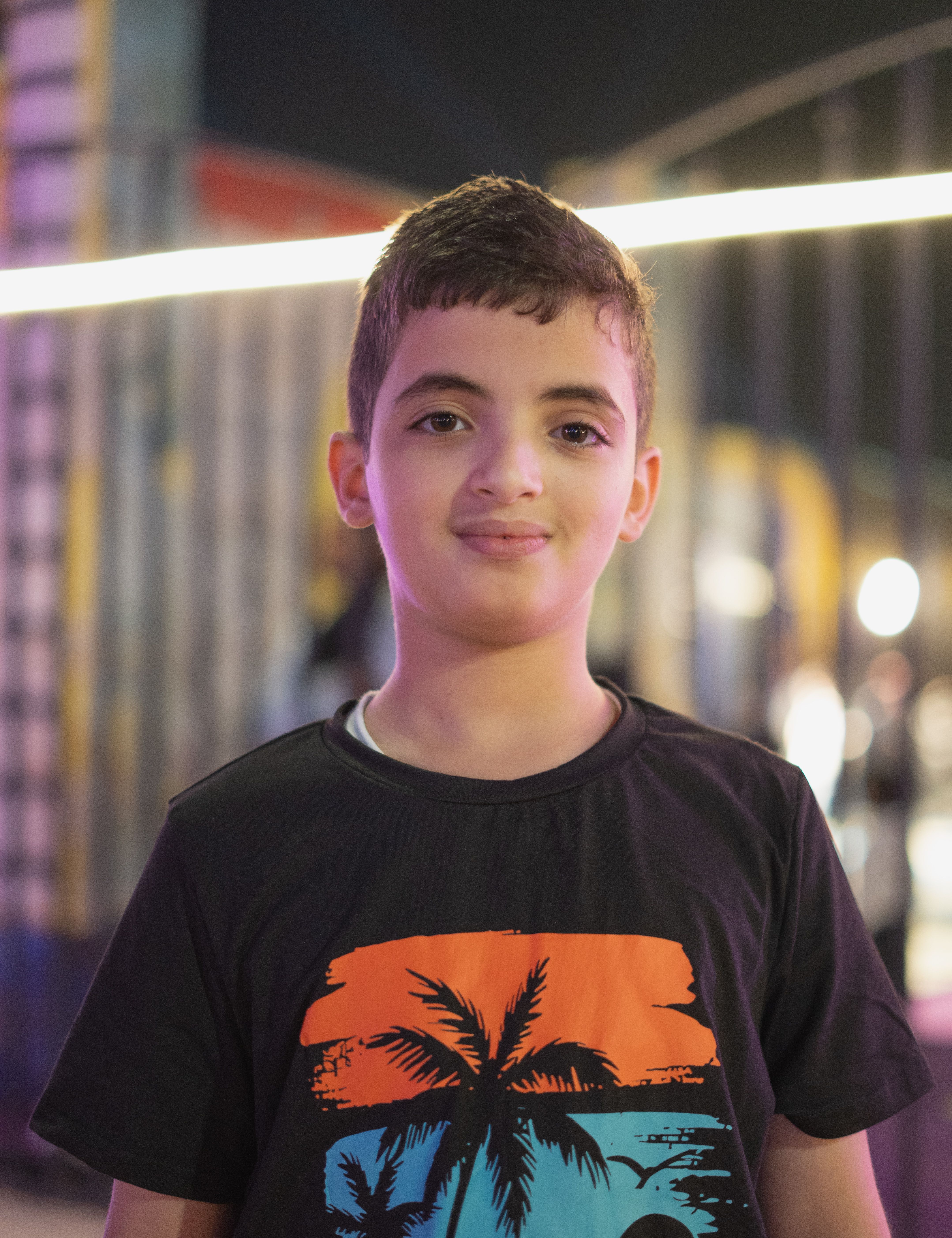 A portrait of a young boy standing outdoors at night with soft lighting.