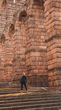 A person stands near the historic Roman aqueduct in Segovia, Spain, showcasing its ancient architecture.