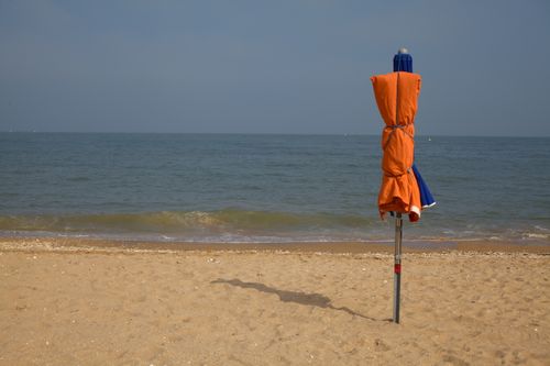Free A folded beach umbrella stands on a tranquil sandy beach by the sea under a clear sky. Stock Photo