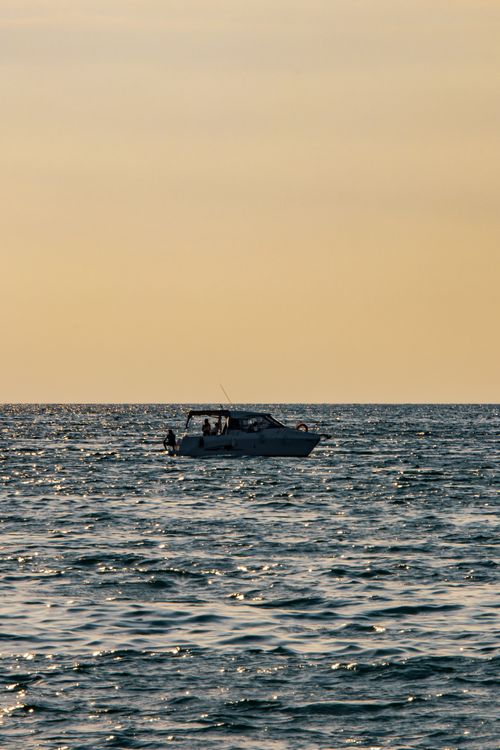 Free A boat sails on the ocean during a serene sunset, capturing a tranquil nautical scene. Stock Photo