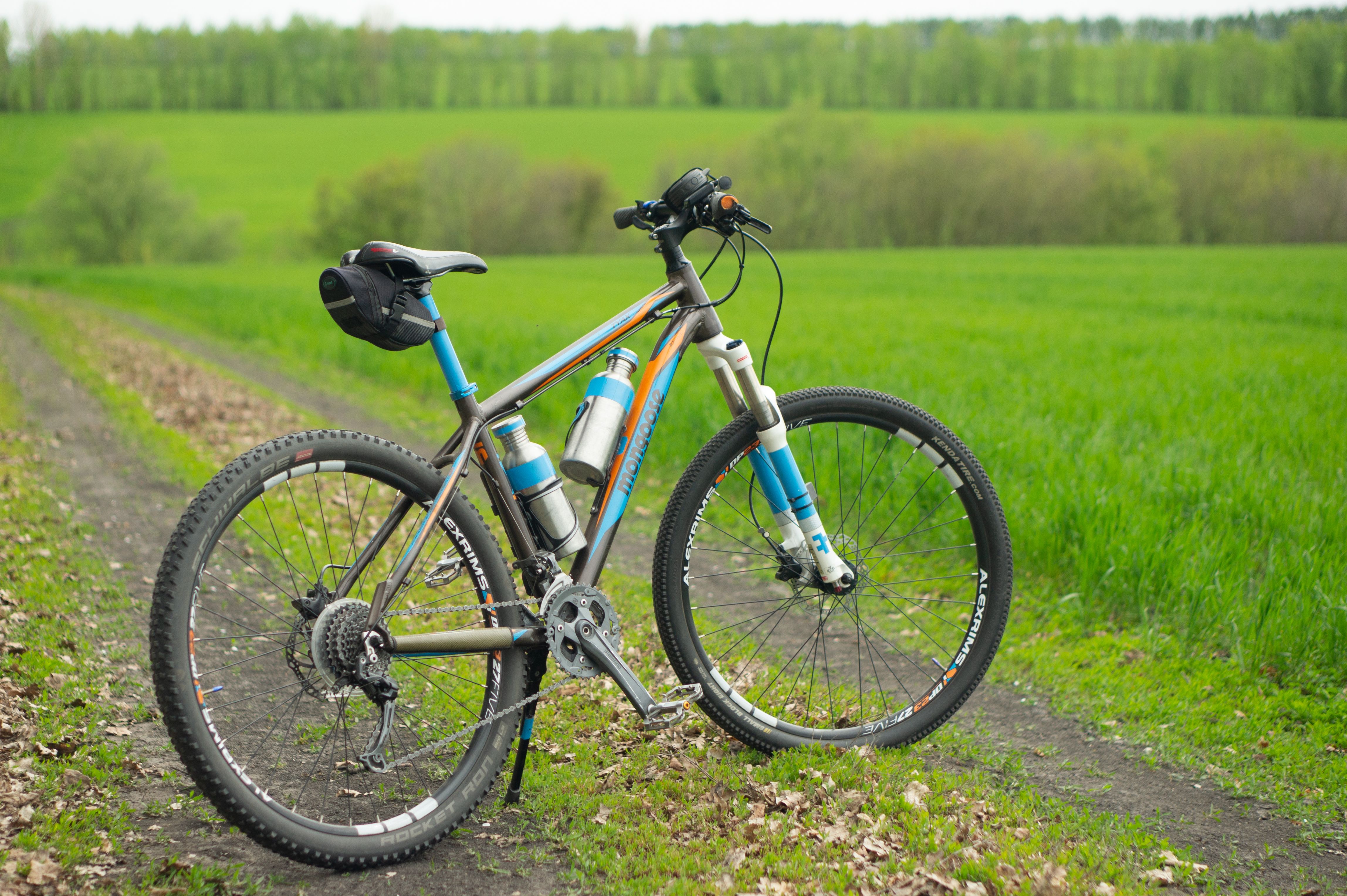 Close-up of a mountain bike on a countryside trail in spring, surrounded by lush green fields.