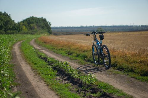 Free A lone mountain bike on a dirt path through scenic rural fields on a sunny day. Stock Photo