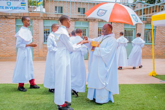 A priest performs a religious ceremony with acolytes in white robes outdoors.