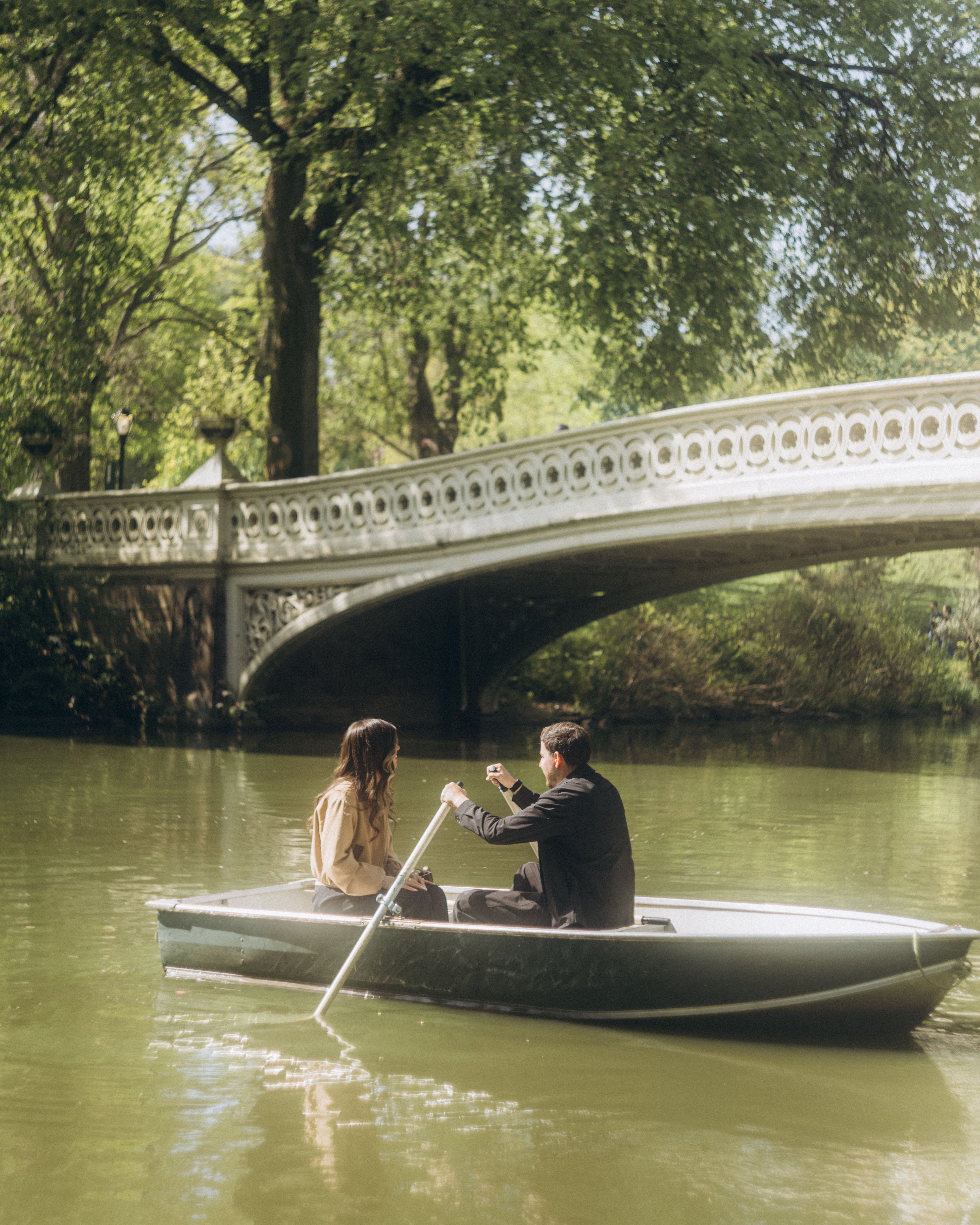 A couple enjoys a peaceful boat ride under a scenic bridge in Central Park.