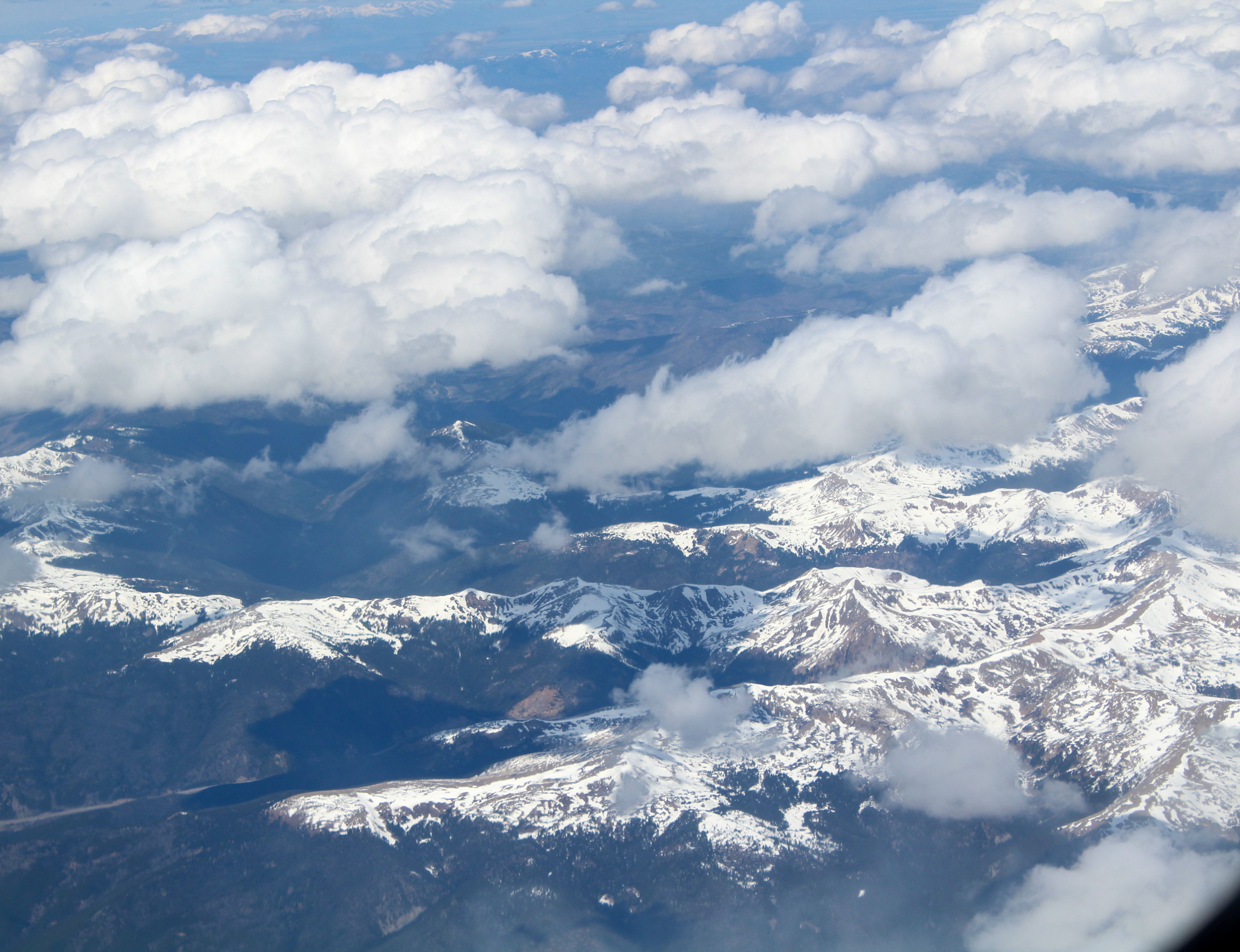 A stunning aerial view of the snow-capped Rocky Mountains under a blue sky with clouds.