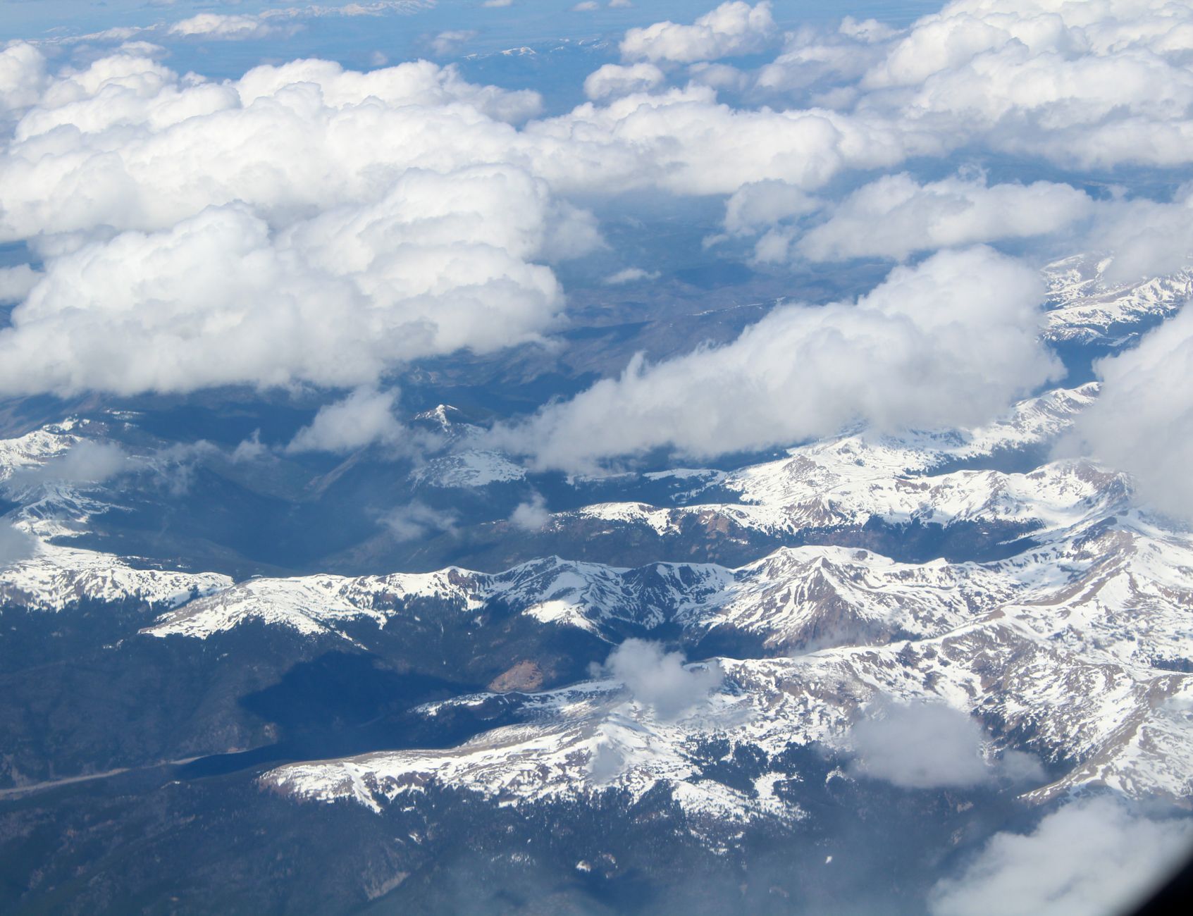 A stunning aerial view of the snow-capped Rocky Mountains under a blue sky with clouds.