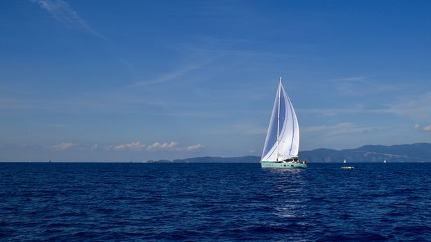 A tranquil yacht cruising on deep blue waters under a clear summer sky.
