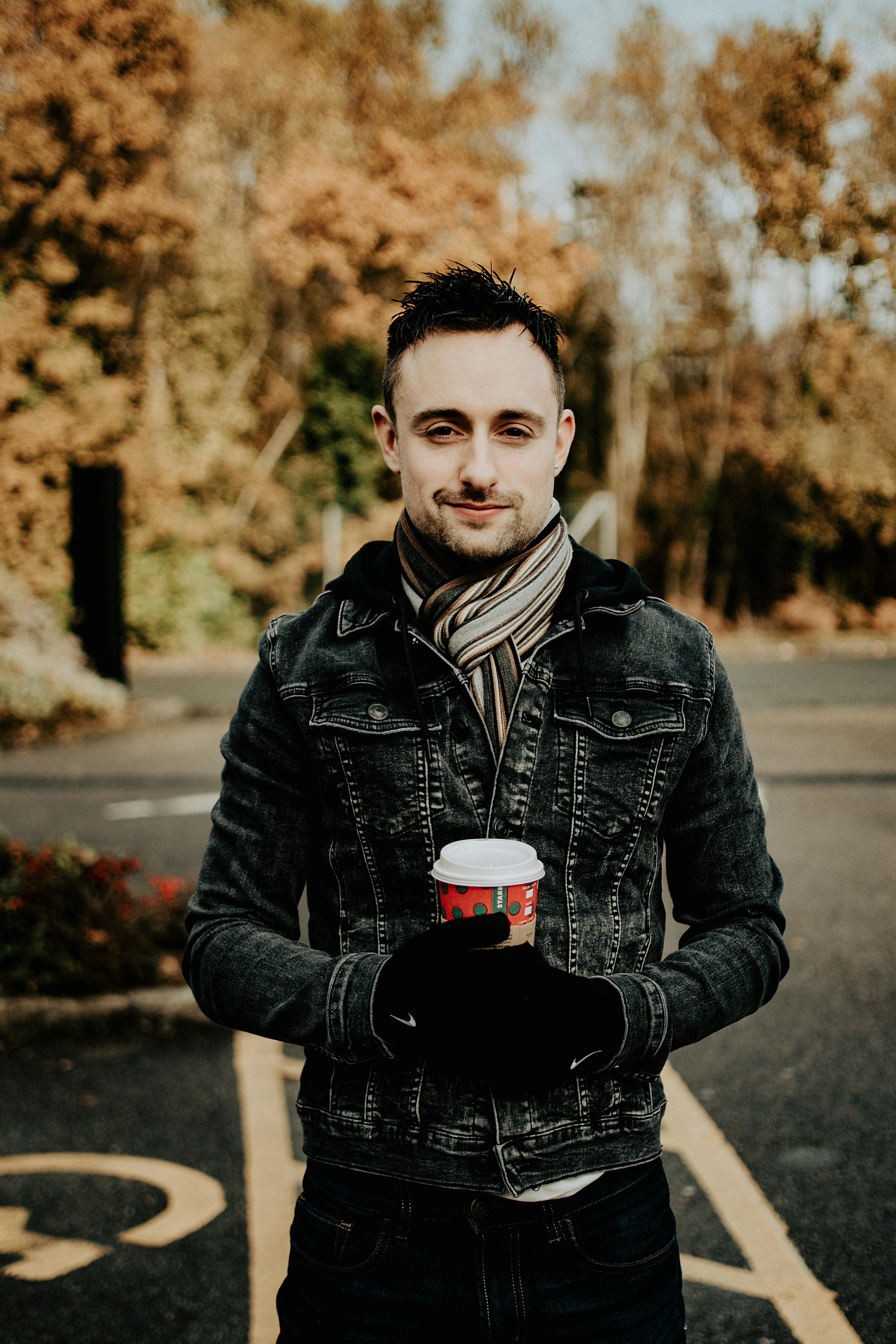 秋天，一名身穿牛仔夹克的男子在户外端着咖啡杯