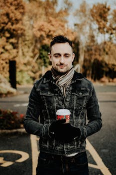 秋天，一名身穿牛仔夹克的男子在户外端着咖啡杯