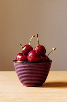A stack of vibrant red cherries in a textured bowl on a wooden table, set against a minimalist backdrop.