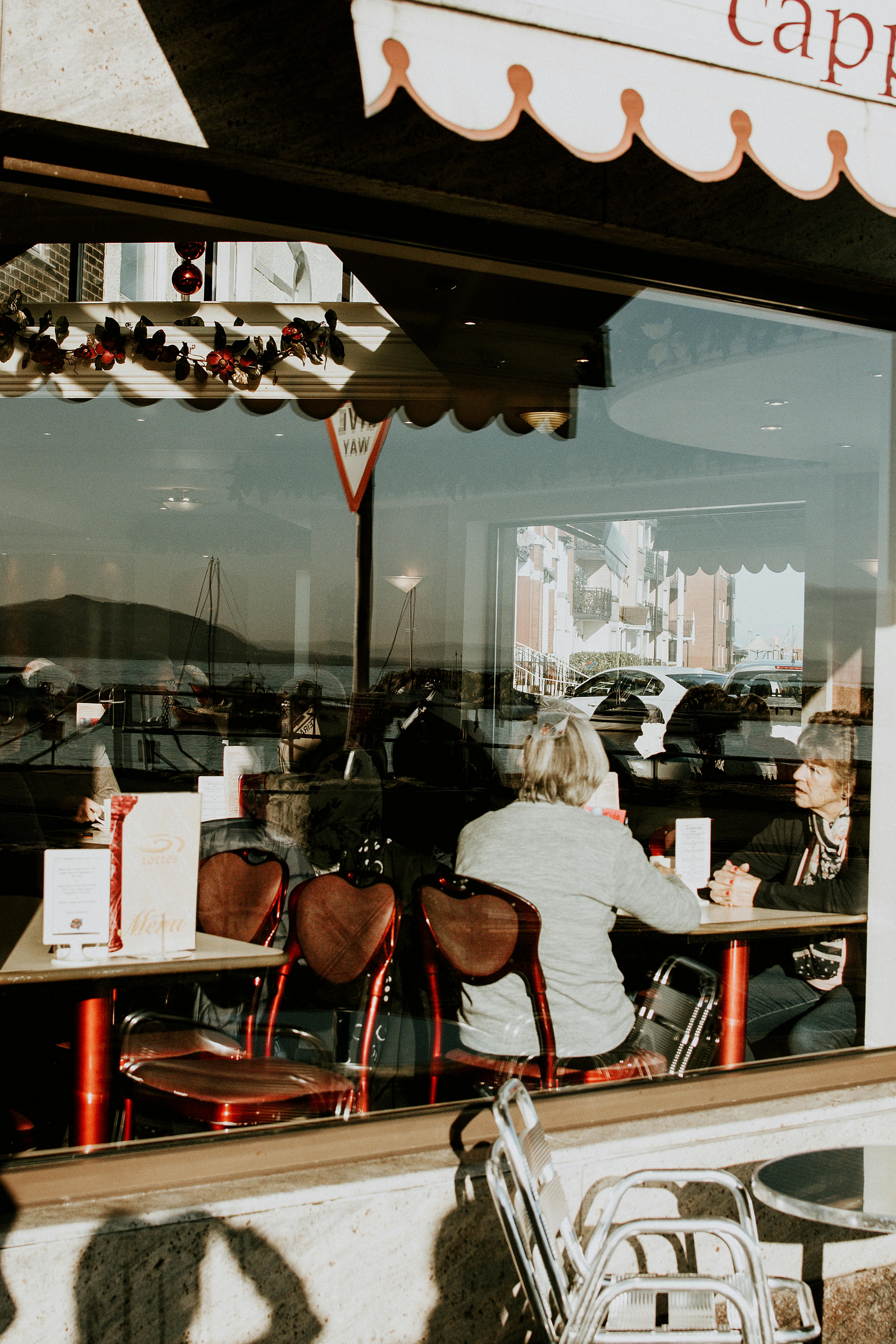 人们在咖啡馆里，透过玻璃欣赏着城市的倒影，享受阳光明媚的一天，捕捉城市的生活方式