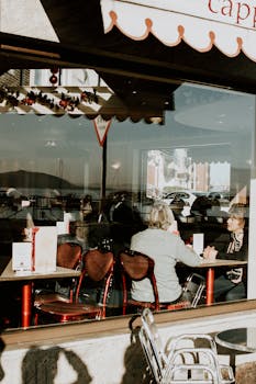 人们在咖啡馆里，透过玻璃欣赏着城市的倒影，享受阳光明媚的一天，捕捉城市的生活方式