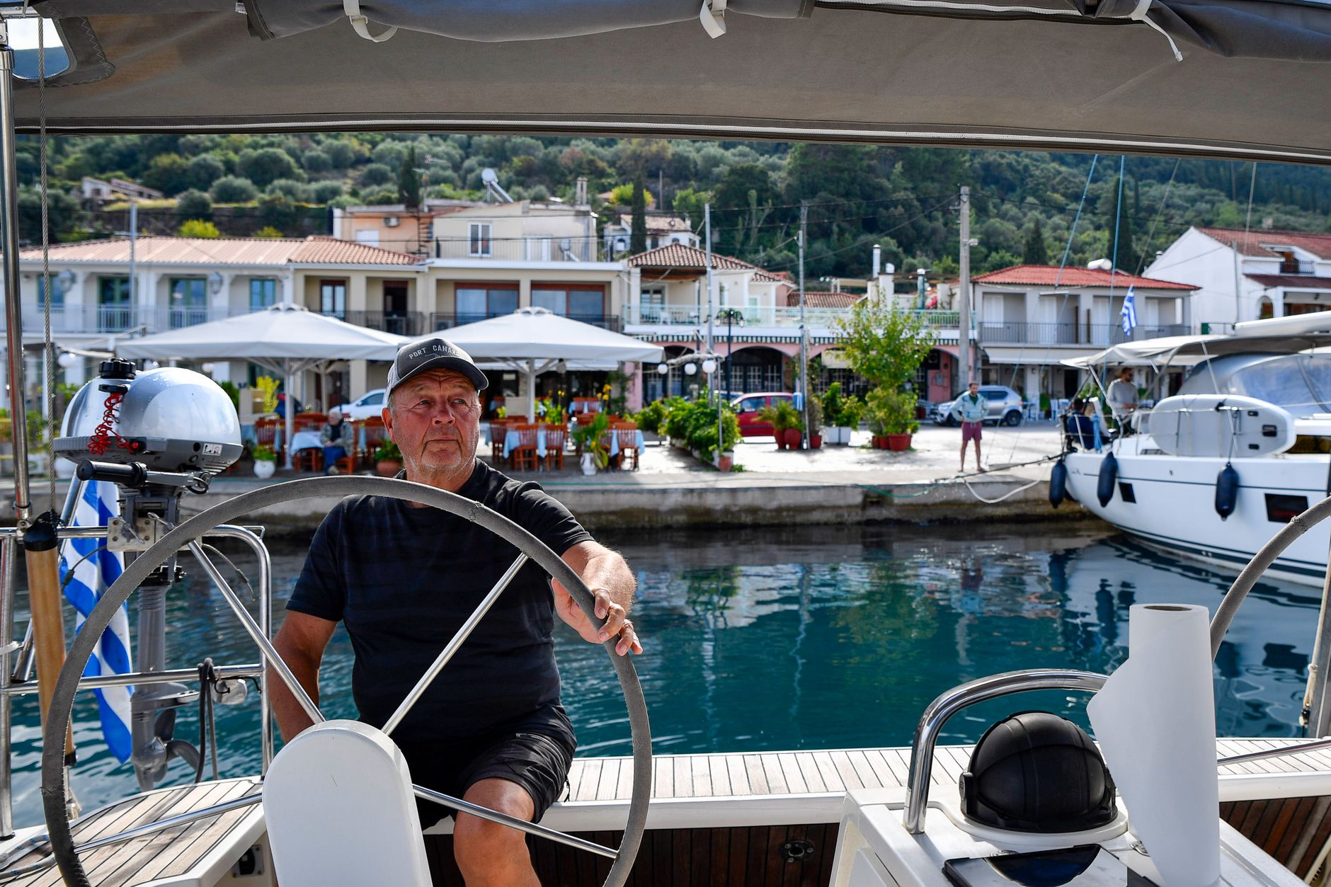 A senior skipper expertly navigates a yacht in a picturesque Greek harbor, embodying the maritime lifestyle.