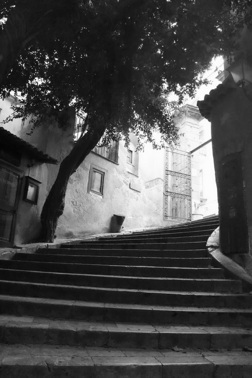Free Black and white image of a steep, curved stone stairway lined with houses in Cefalù, Sicily. Stock Photo
