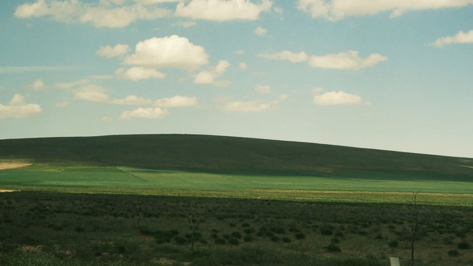 A tranquil scene of a lush green landscape under a blue sky with fluffy clouds.
