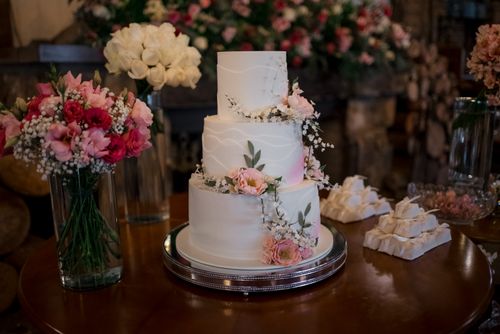 Free Elegant three-tier wedding cake adorned with pink and white flowers, surrounded by beautiful floral arrangements. Stock Photo