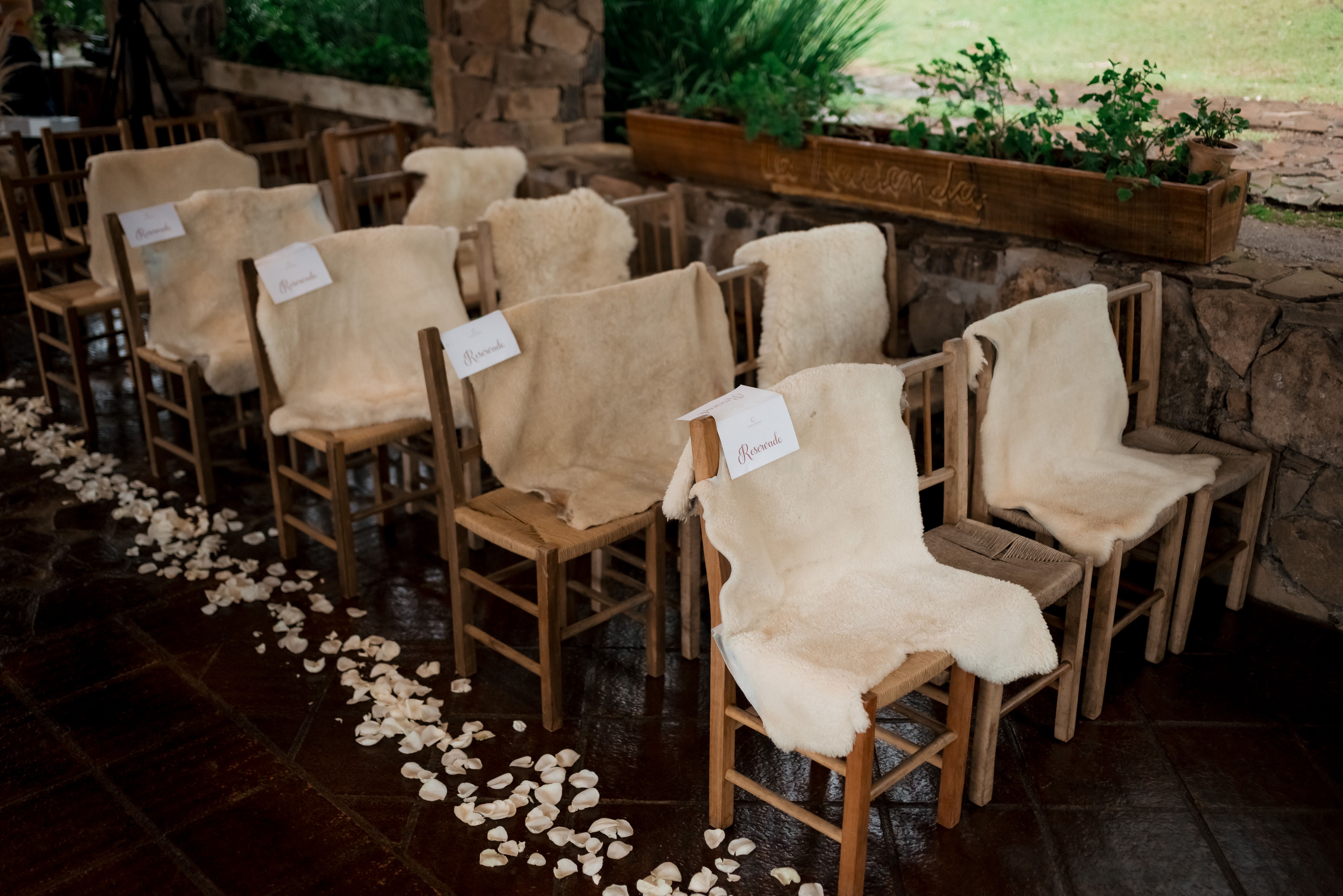 Cozy wedding seating arrangement outdoors with wooden chairs and soft fur covers.