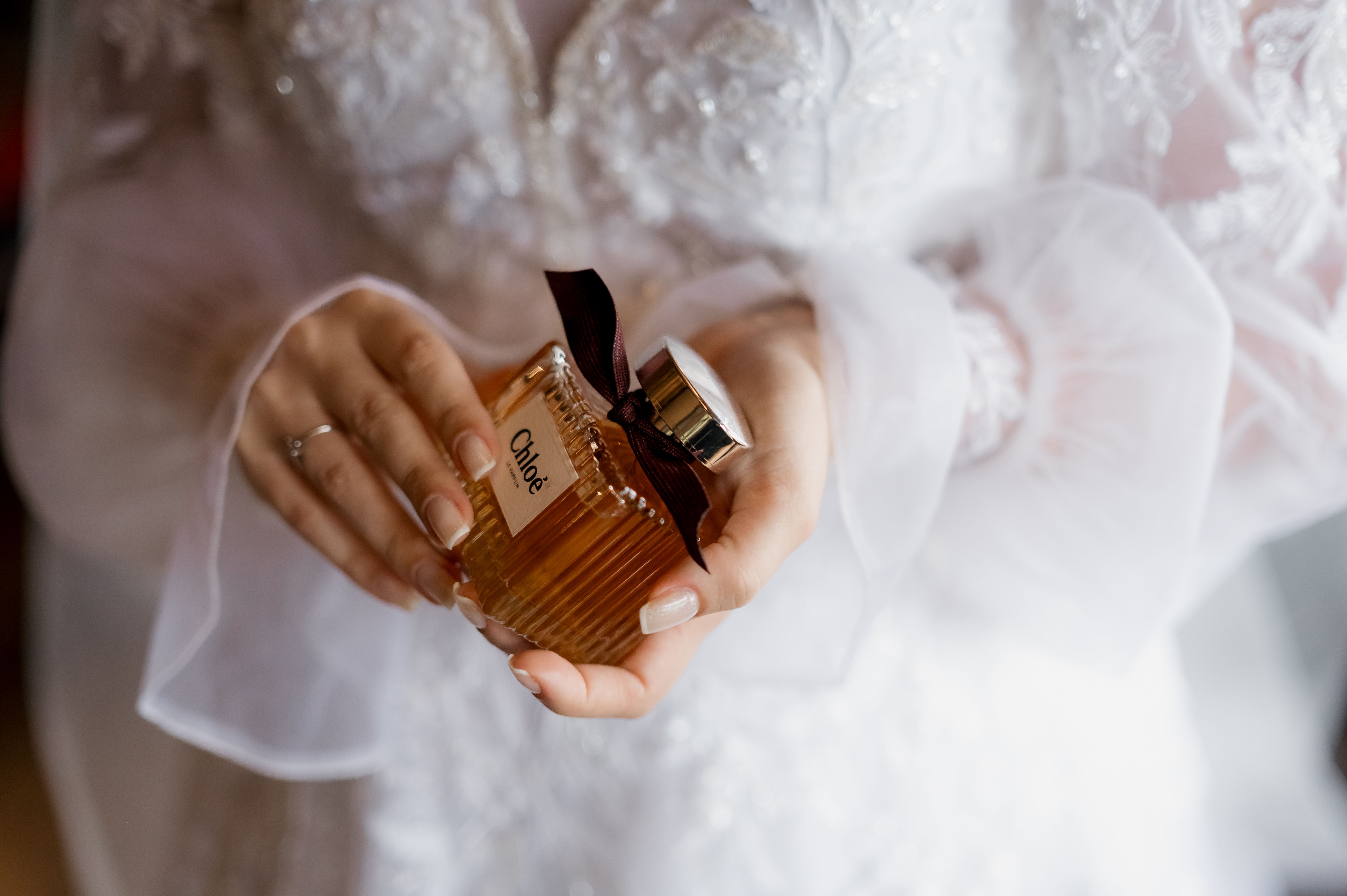 A bride in white lace dress holding a luxury Chloe perfume bottle, symbolizing elegance and style.