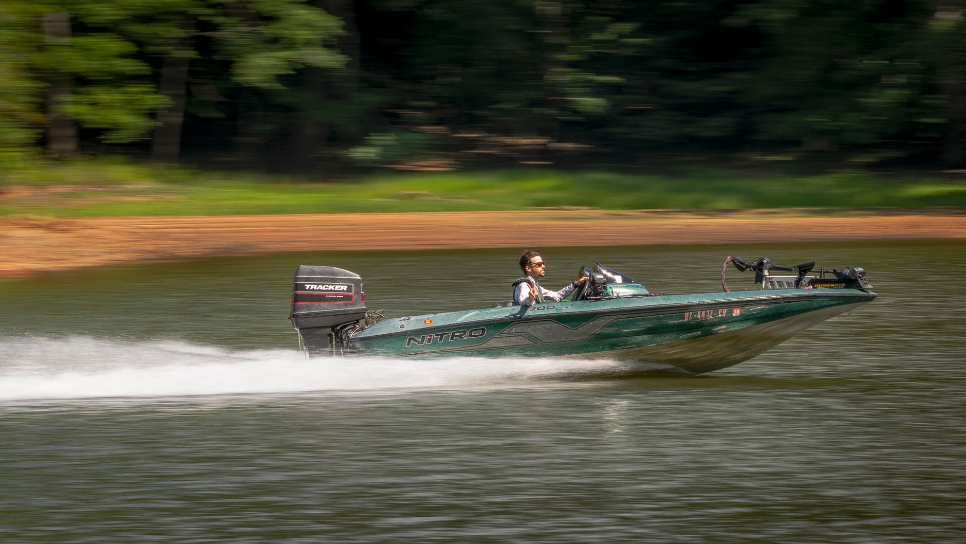 A man driving a fast motorboat on a serene lake surrounded by greenery.