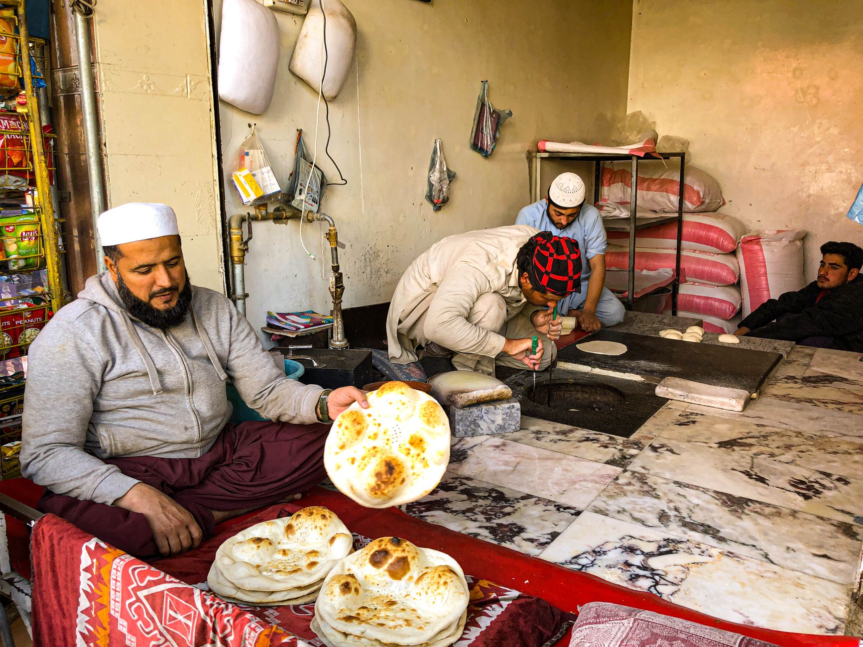 Local bakers in Mingora, Pakistan, crafting traditional naan bread in a bustling bakery.