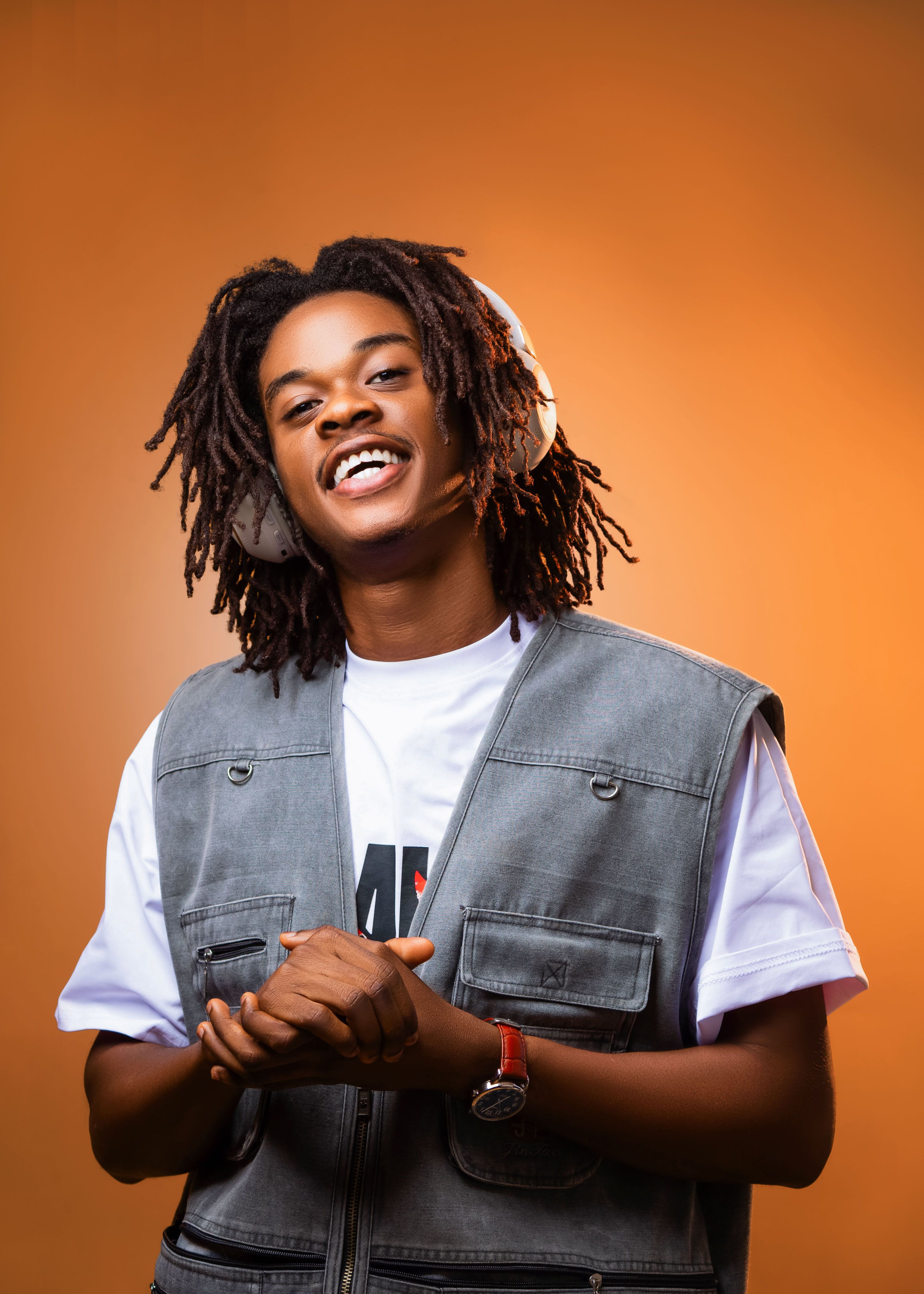 Smiling young African man with headphones enjoying music against a warm orange background.