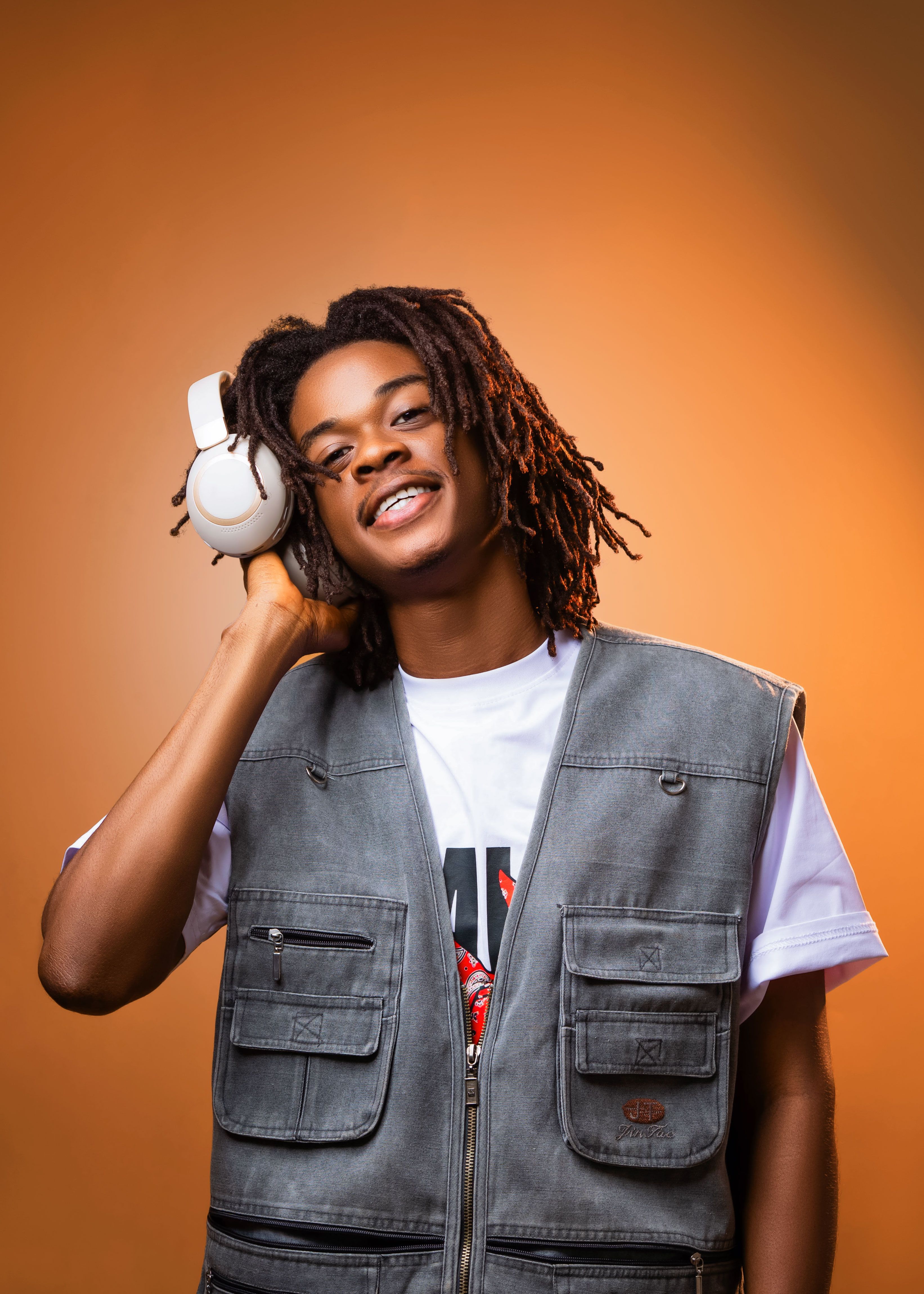 Smiling young man with headphones in Ghana enjoying music on an orange background.