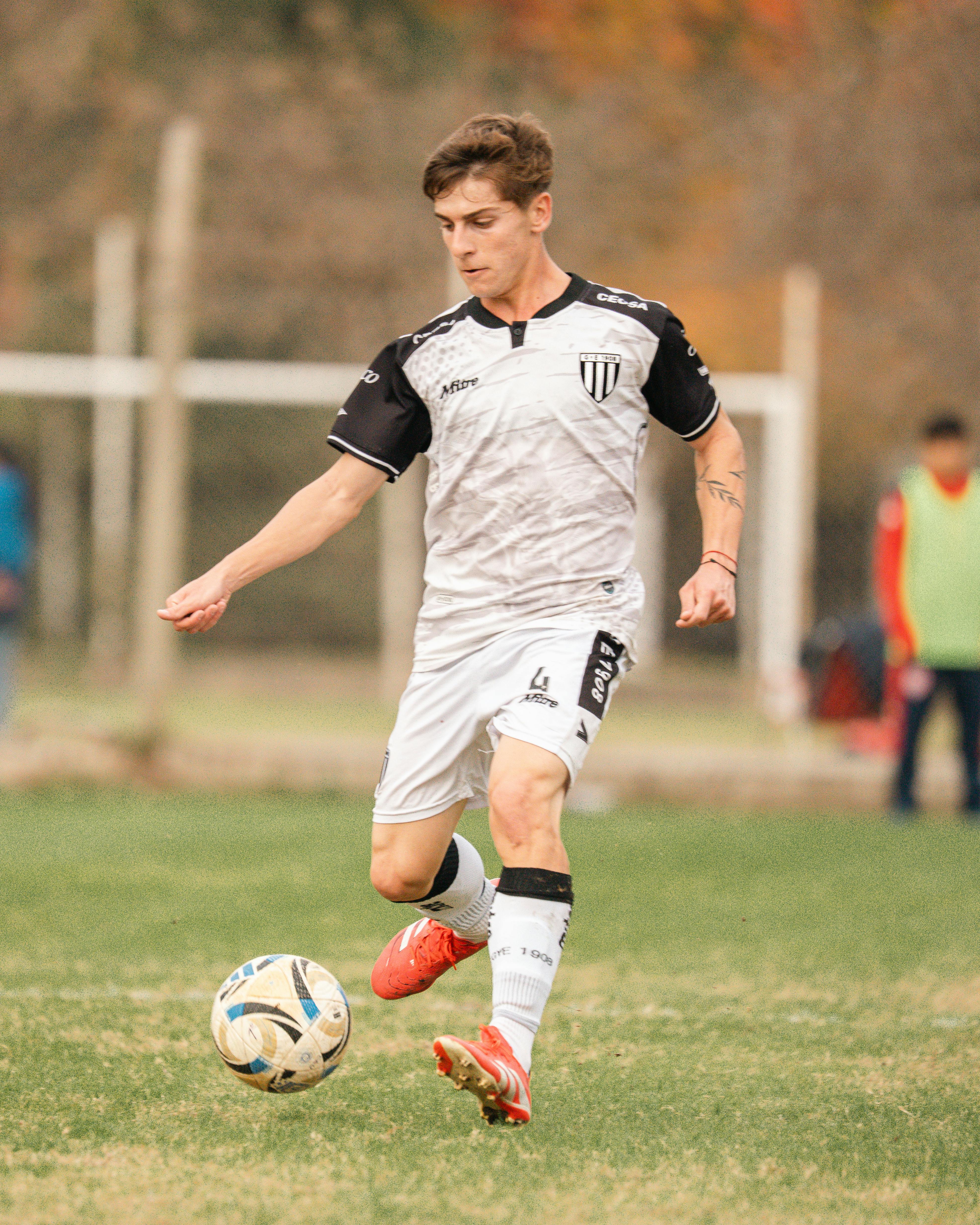 Young male soccer player in action on grassy field during daytime match.
