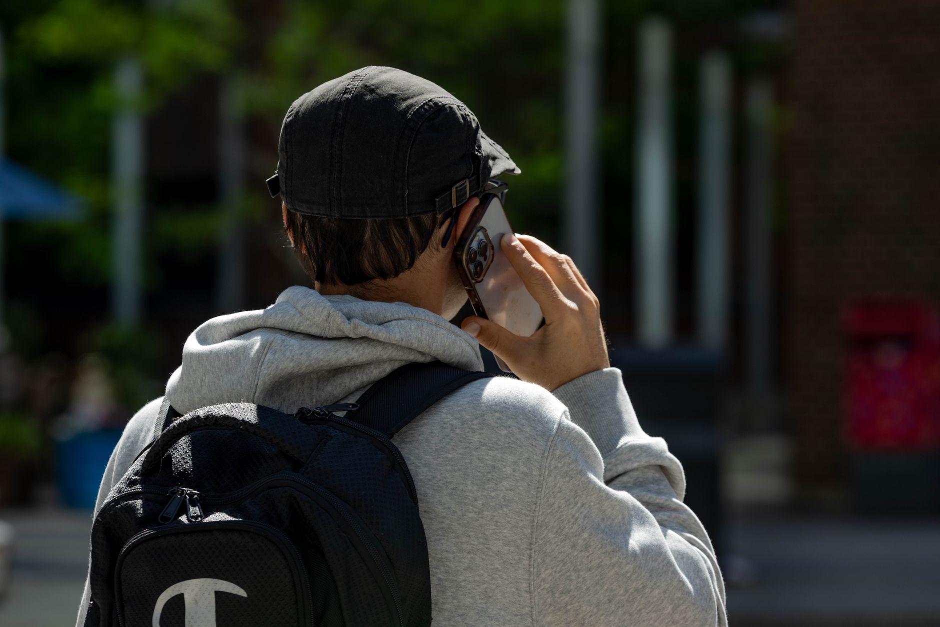 Back view of a man in a cap with a backpack talking on a smartphone outdoors.
