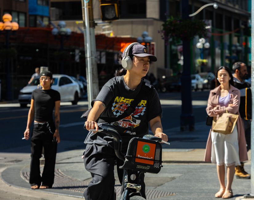 Young cyclist wearing headphones rides through city streets on a sunny day.