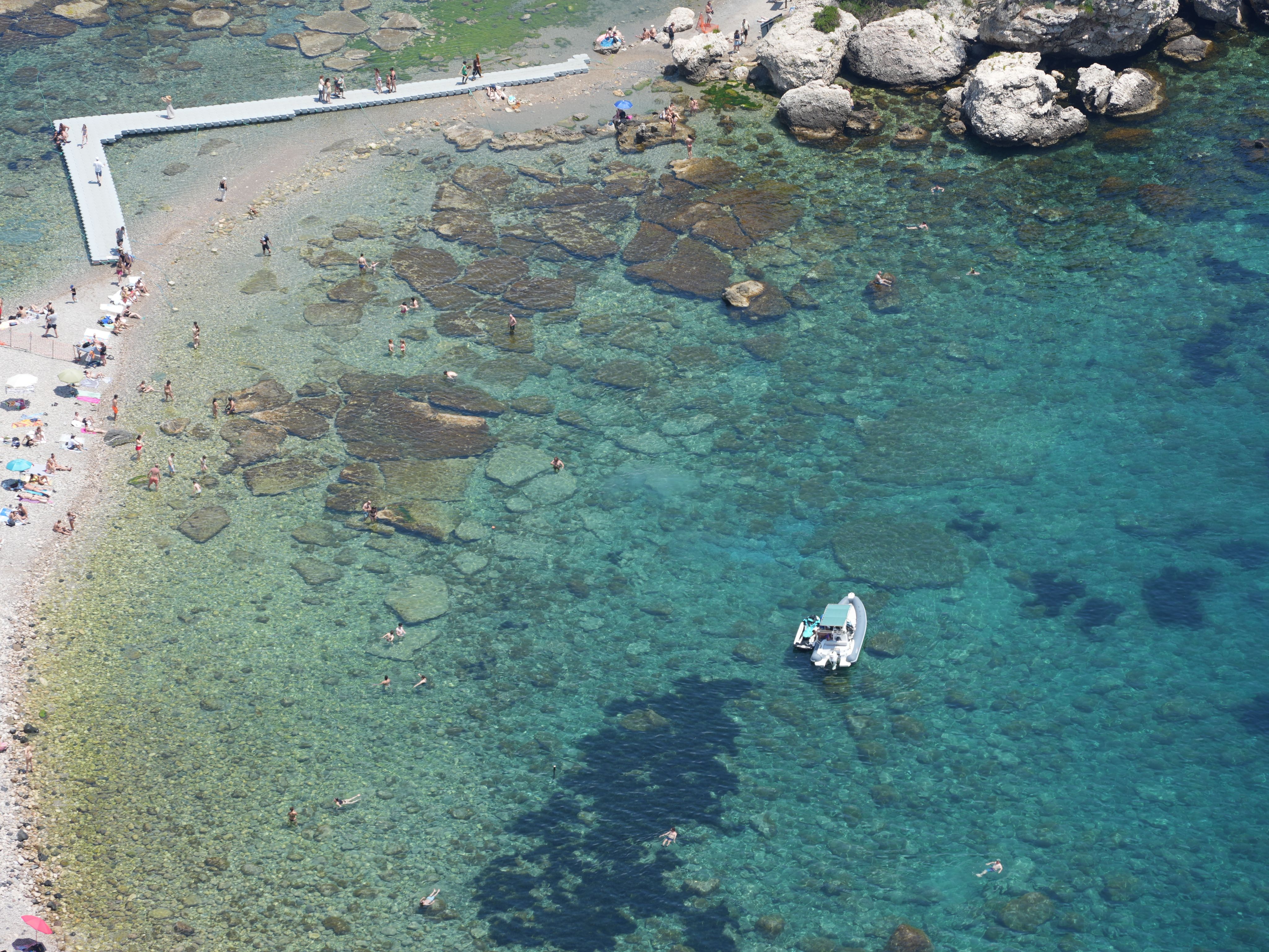Stunning aerial shot of a beach in Sicily, Italy, with clear turquoise waters and sunbathers.