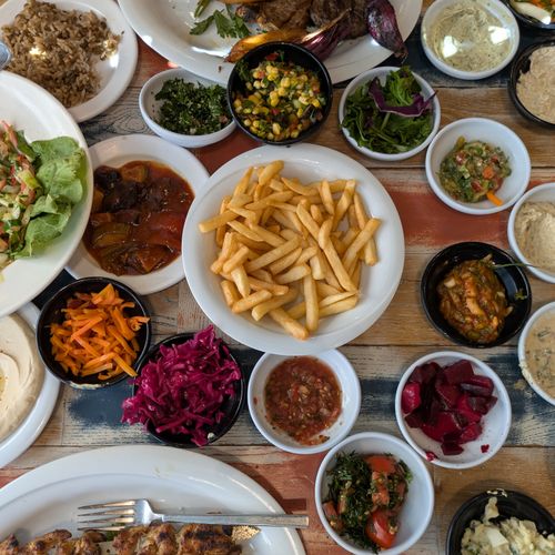 Free Delicious spread of Middle Eastern mezze with fries, salads, and dips on a wooden table. Stock Photo