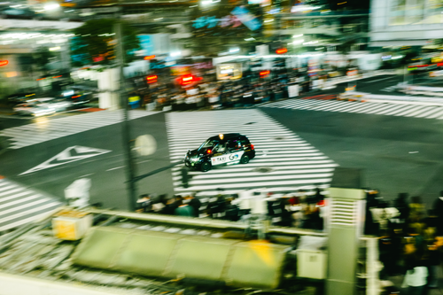 Free A taxi speeds through Shibuya Crossing at night, capturing Tokyo's vibrant energy. Stock Photo
