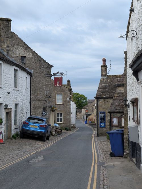 Free Quaint English village street with stone buildings and parked car on a cloudy day. Stock Photo