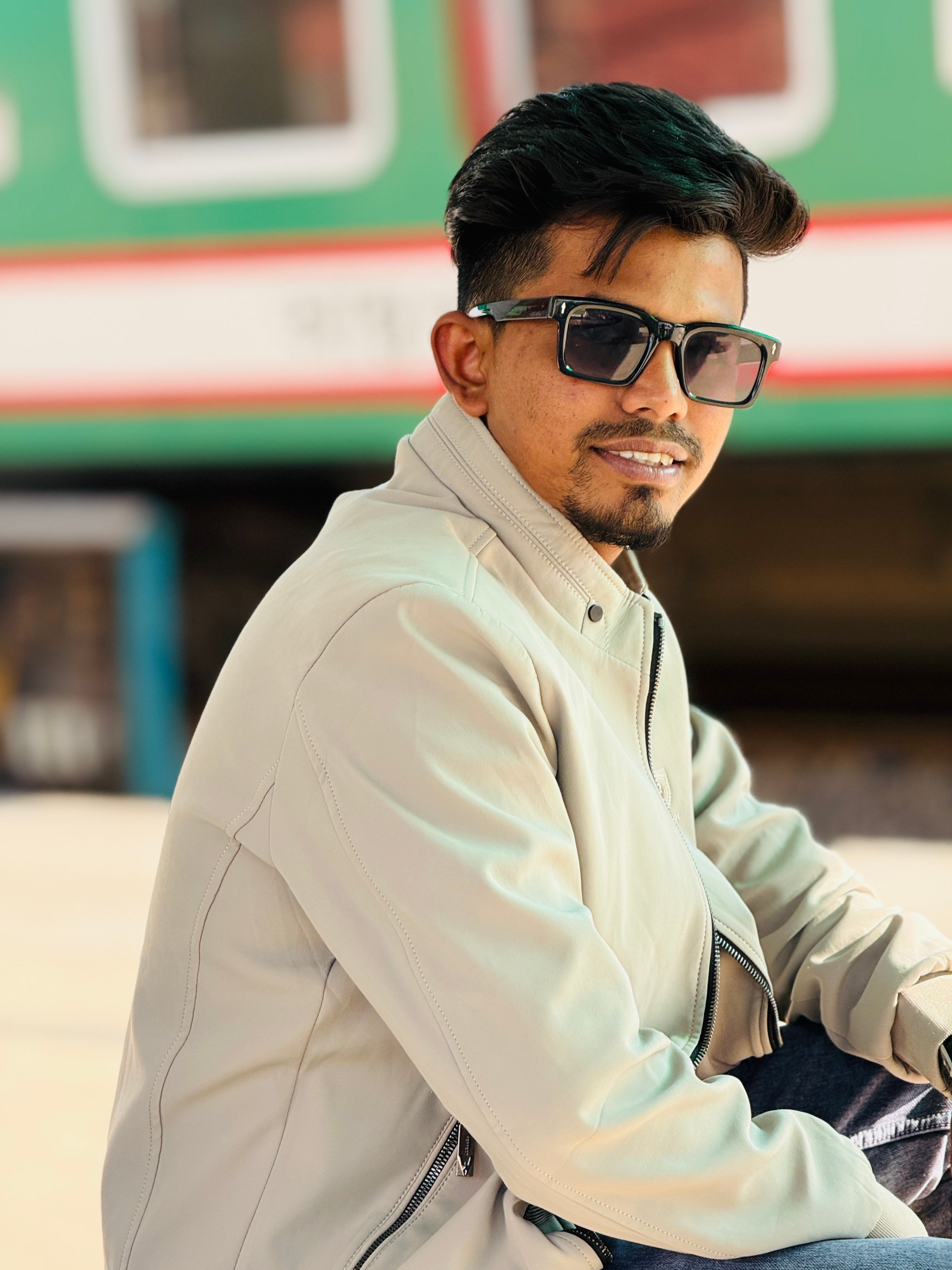 Fashionable young man in sunglasses posing confidently by a train outdoors.
