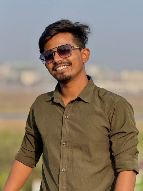 Free A young man wearing sunglasses and a green shirt smiles outdoors on a sunny day. Stock Photo