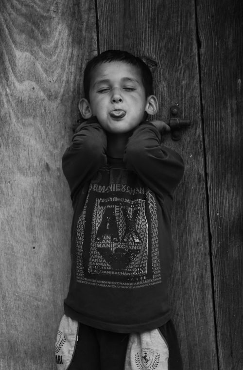 Free Black and white photo of a playful child sticking out tongue in front of a wooden door, exuding innocence and fun. Stock Photo