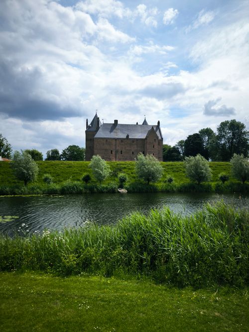 Free Peaceful castle scene with vibrant greenery and a tranquil river under cloudy skies. Stock Photo