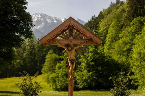 Free Wooden crucifix set against a lush green forest and distant snowy mountains. Stock Photo